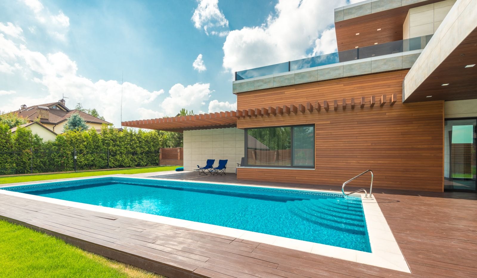 Rectangular inground pool with wood decking beside a modern home